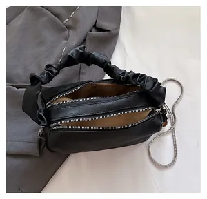 Detail view of double zipper pockets and pleated handle on black crossbody bag