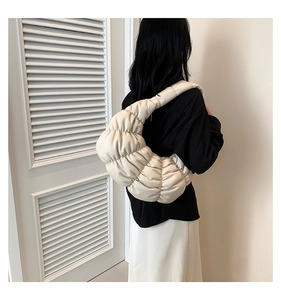 Detail view of the pleated cream white cloud bag's texture and puffy shape on shoulder