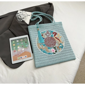 Detail of light blue straw tote with traditional Chinese dragon embroidery and silk tassel