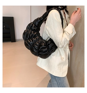 Detail of elegant black pleated cloud bag texture held by model in stylish setting