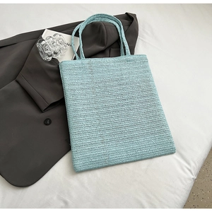 Detail of light blue straw woven tote bag with herringbone texture on grey blazer