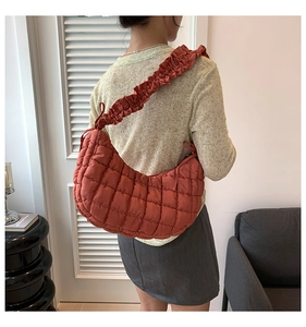 Detailed view of rust red quilted dumpling bag featuring a ruffled shoulder strap