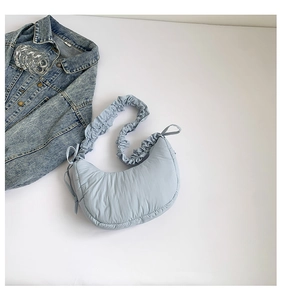 Detail of light blue quilted shoulder bag with ruffle strap and bow tie decoration