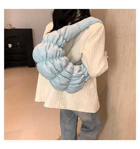 Detailed back view of a soft light blue pleated cloud bag worn by a model in a minimalist room