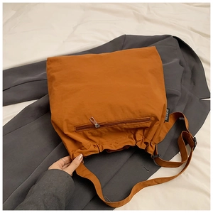 Detail of orange nylon tote bag showing front zipper pocket and wide fabric strap