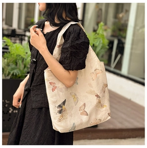 Detailed view of beige tote bag with colorful butterfly prints in a casual outdoor setting