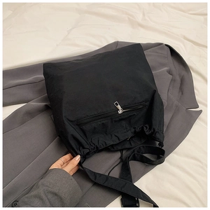 Detail of a black nylon shoulder bag with silver zipper on a gray suit jacket
