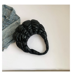 Detailed top view of a black pleated cloud bag on white surface with denim accessory