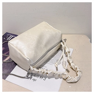 Detail view of beige ruched handbag with floral embroidery and silver chain strap