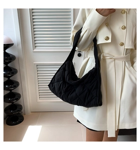 Detalle de bolso acolchado negro con relleno suave y correa integrada sobre abrigo beige