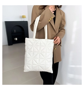 Close-up of white quilted tote bag worn with a brown blazer in a minimalist indoor setting