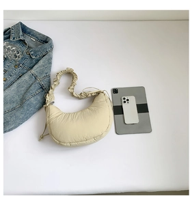 Flat lay of beige crescent nylon bag with scrunchie strap next to a tablet and denim