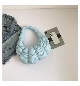 Detail view of a light blue pleated cloud bag styled with lifestyle accessories