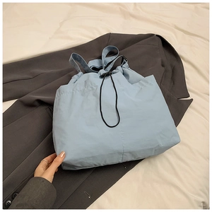 Detail of light blue nylon tote bag with drawstring closure on a grey suit background