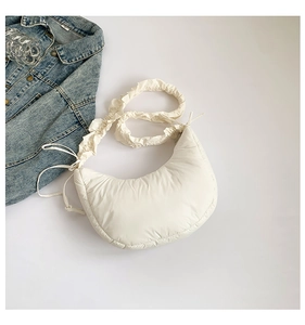Detail of white quilted half-moon bag with ruffled shoulder strap and side drawstring