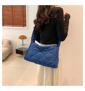 Sac à bandoulière matelassé bleu avec motif losange porté par un mannequin en intérieur