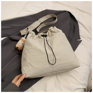 Detail of cream drawstring tote bag with plush charm on a grey blazer background