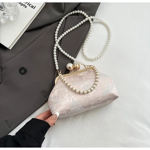 Detailed close-up of champagne silk brocade embroidery and dual pearl clasps on a handbag
