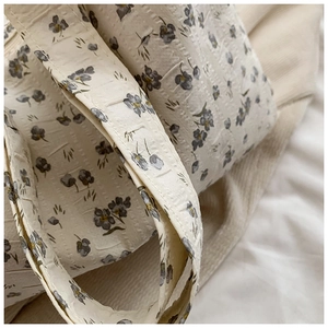 Gros plan sur les petits motifs floraux gris sur le tissu texturé crème du sac