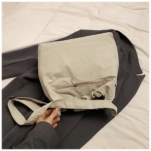 Detail of beige large tote bag with zipper pocket and adjustable strap on a blazer