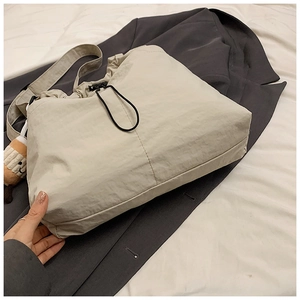 Detail of cream nylon tote bag with drawstring closure and brown plush pendant
