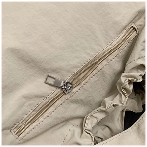 Macro view of silver zipper and ruffle detail on a beige lightweight nylon tote bag