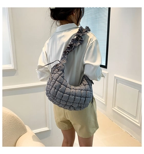 Close-up of a dark grey quilted crescent shoulder bag with stylish ruffled strap details
