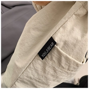 Detail view of the woven 'YOU JI BEAR' brand label on beige nylon tote bag fabric