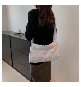Détail du sac à bandoulière matelassé blanc à losanges porté par un mannequin en scène