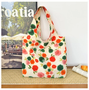 Close-up of a floral canvas tote bag featuring red and pink blossoms on a wooden desk