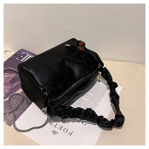 Detailed view of black pleated cylinder handbag with floral texture and chain strap