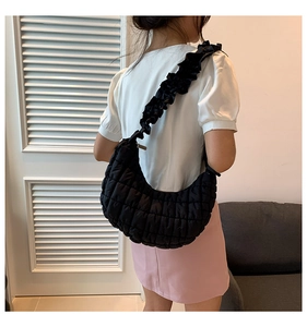 Detail of quilted croissant bag with ruffled shoulder strap worn by a model