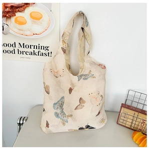 Close-up of beige canvas tote bag featuring colorful realistic butterfly prints and lifestyle setup