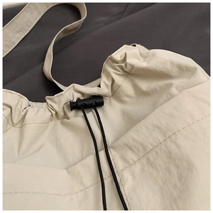 Detail of beige nylon tote bag featuring a black drawstring toggle and neat stitching