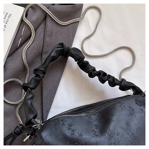 Detail of black pleated shoulder bag with silver chain strap and embossed texture