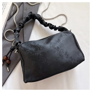 Detail of black pleated handbag with floral texture, silver chain, and beaded tassel