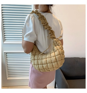 Close-up of quilted beige dumpling bag with ruffled shoulder strap worn by a model