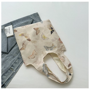 Detail of a beige canvas tote bag with colorful butterfly prints and soft fabric handles