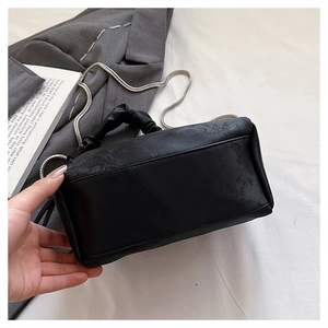 Close-up of black ruched handbag with embossed floral patterns and silver chain strap