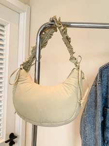 Beige crescent underarm bag with pleated strap and drawstring detail on a hanger