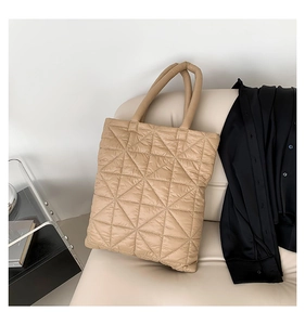 Close-up of beige quilted puffer tote bag with diamond stitching on a leather sofa