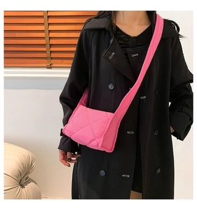 Detail van een felroze gewatteerde crossbodytas met puffer-textuur op een zwarte jas