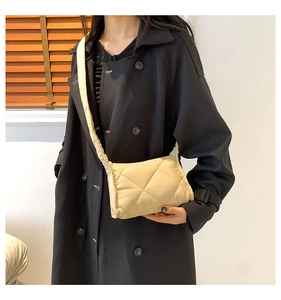 Detail van een beige gewatteerde crossbodytas met brede riem op een model met een zwarte jas
