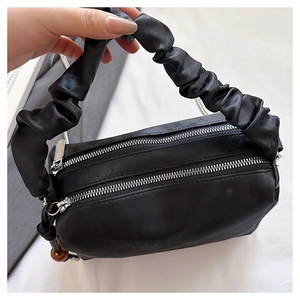 Detail of black pleated handle handbag with double zipper closure and silver chain strap