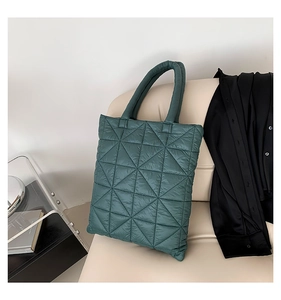 Detail shot of a dark teal quilted puffer tote bag with triangular stitching on a leather seat