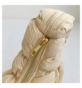 Detailed macro view of gold metal zipper and pleated beige fabric on a crossbody bag