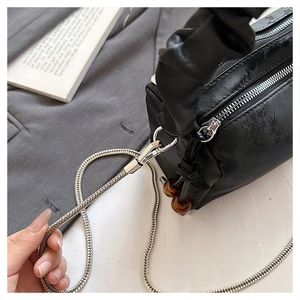 Macro view of black pleated bag featuring silver metal zipper and amber bead pendant
