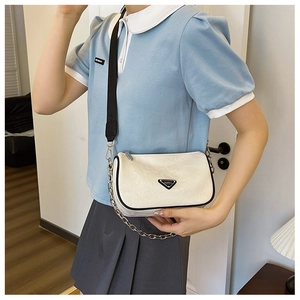 Close-up of white wrinkled leather pillow bag with wide black strap and silver chain detail