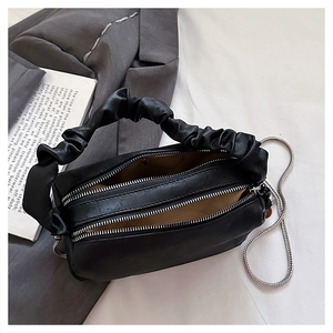 Close-up of black pleated handle handbag with dual zippers and silver chain strap
