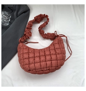 Close-up of terracotta quilted crescent bag featuring stylish pleated shoulder strap detail
